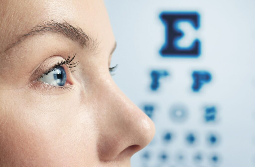A close-up view of a woman's face. The woman is standing in front of a Snellen eye chart.