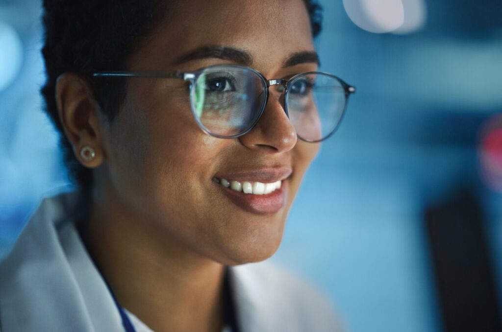 Woman wearing computer glasses, smiling while looking at a computer screen, reducing eye strain with proper eyewear.