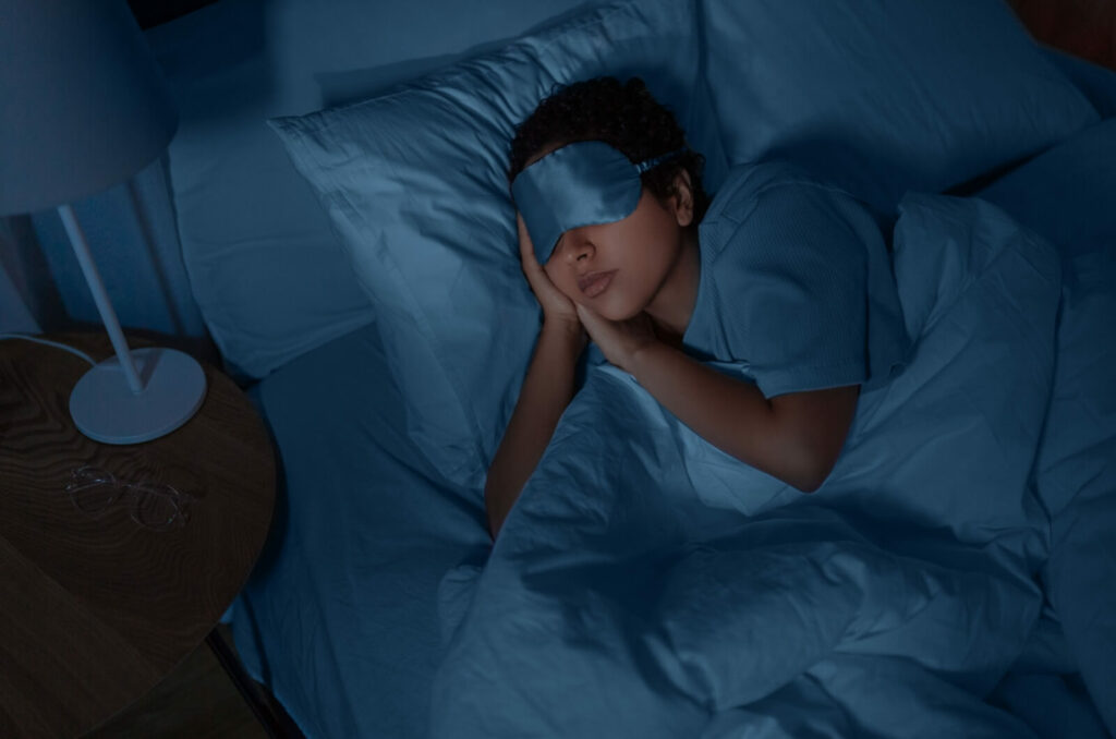 A person with a satin blue eye mask sleeping under a duvet