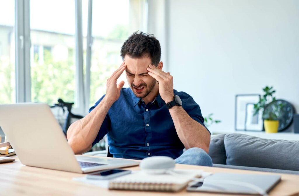 A person trying to work rubs their head due to a headache from poor vision.