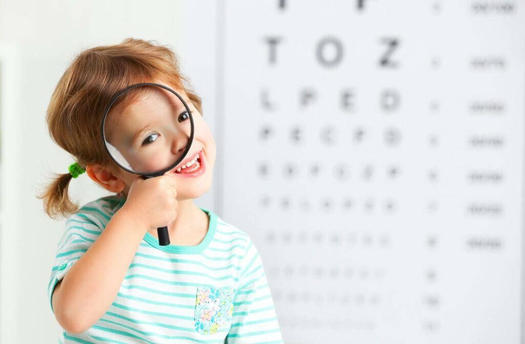 A child sitting in front of an out-of-focus eye chart looks through a magnifying glass.
